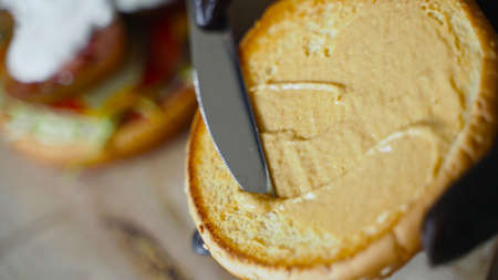 Chef in black gloves smears a bun with mustard for hamburger.の写真素材