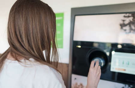 Woman puts bottle in automatic bottle recycling machine. Reverse vending recycling machine.の写真素材