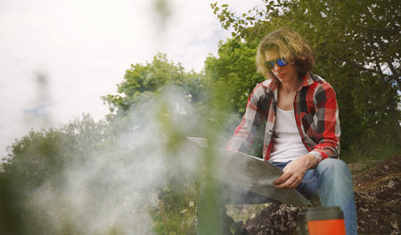 Man with map sits in front of bonfire in the forest.