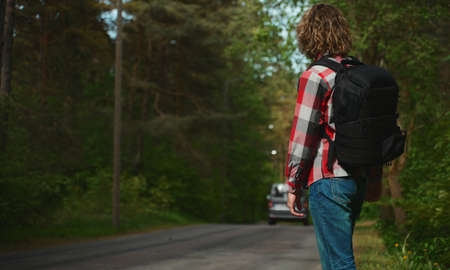 Man with backpack catching a car on the road. Travel by autostop.の写真素材