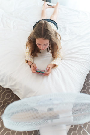 Teenager lies with the phone in front of cooling fan.