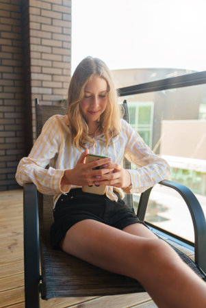 Teenager sitting with the phone on the balcony.