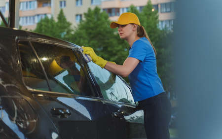 Woman in uniform cleaning car with sponge. Car wash service.の写真素材