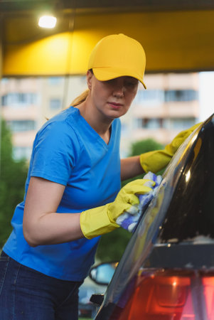 Woman in uniform cleaning car with sponge. Car wash service.