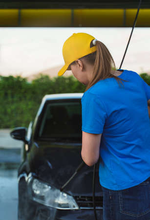 Woman in uniform cleaning car using high pressure water. Car wash service.の写真素材