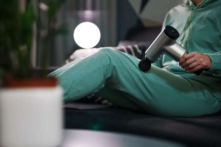 Woman massaging leg with massage percussion device at home.の写真素材