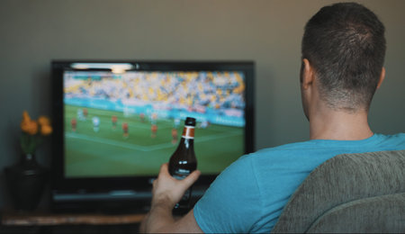 Man with bottle of beer watching football on TV.