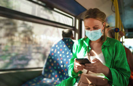 Woman in medical mask with mobile phone in the bus.の写真素材