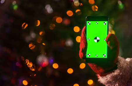 Santa claus holding phone in hand. Green chroma key for your AD.の写真素材