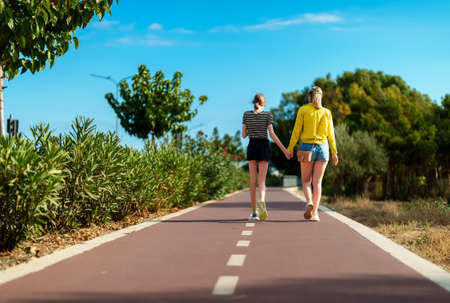Mom and her daughter walk along the footpath in summer.の写真素材