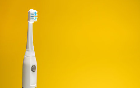 Electric ultrasonic toothbrush on yellow background.
