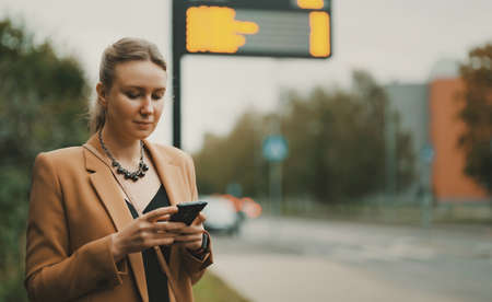 Woman with smartphone is waiting for bus at bus stop.の写真素材