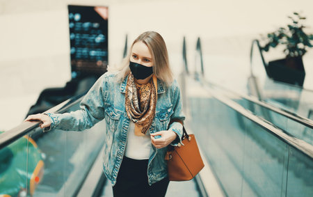 Woman in medical mask rides an escalator in shopping center.の写真素材