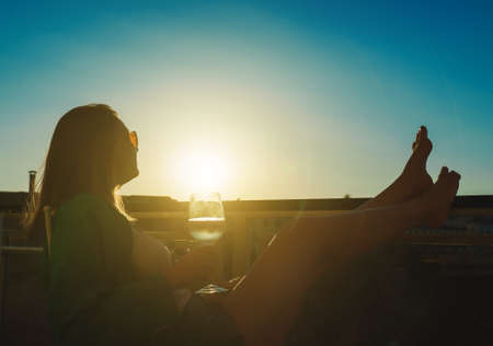 Woman with white wine enjoys the sunset on her balcony.の写真素材
