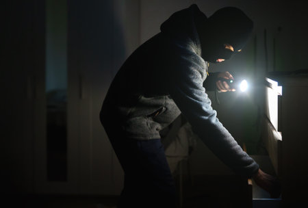 Masked robber with flashlight torch checking apartment.の写真素材