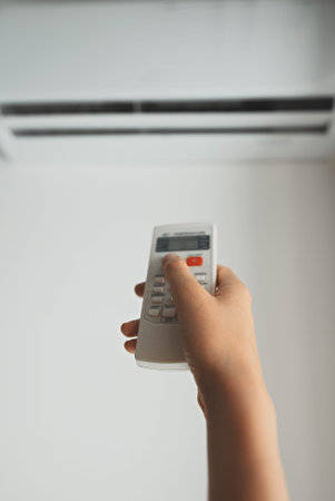 Teenage girl holding remote control aimed at the air conditioner.