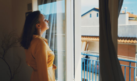 Woman enjoys warm summer breeze while standing in front of the window.の写真素材