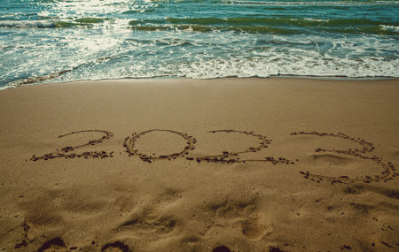 Year 2023 handwriting on sand beach surface.