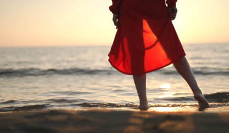 Woman in red stands in the sea at sunset.の写真素材