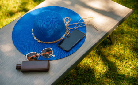 Blue hat, sunscreen, phone and sunglasses on a sun lounger.