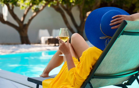Woman with white glass of wine relaxing near swimming pool.の写真素材