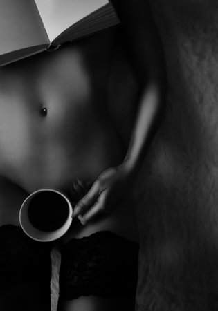 Naked woman lies on a bed with a cup of coffee and book. Art photo.の写真素材