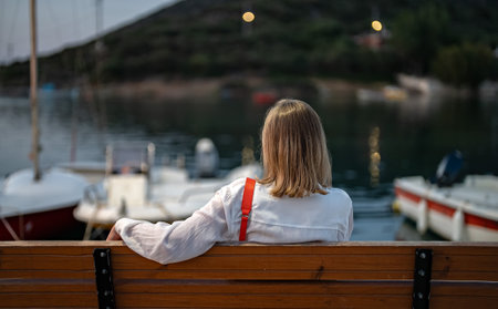 Woman sits on a bench and looks at the bay with boats.の写真素材
