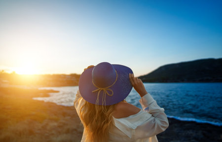 Woman in a blue hat at sunset by the sea.の写真素材