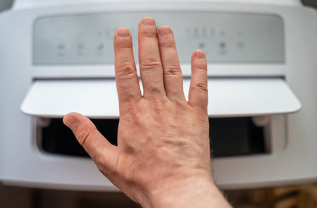 Male hand checking air flow of floor standing mobile air conditioner.