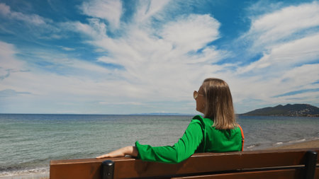 Woman in a green dress sits on a bench on the seashore.の写真素材