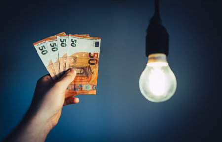 Man holds money next to a light bulb. Expensive electricity concept.