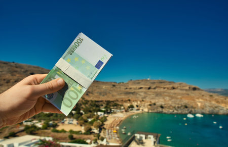 Man holds money against the backdrop of a beach in a warm country.