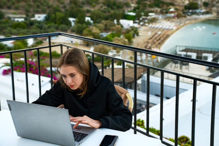 A young girl uses a laptop on the balcony at sunset.