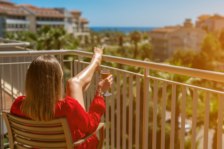 Woman in red dress with white wine enjoying vacation at balcony.の写真素材