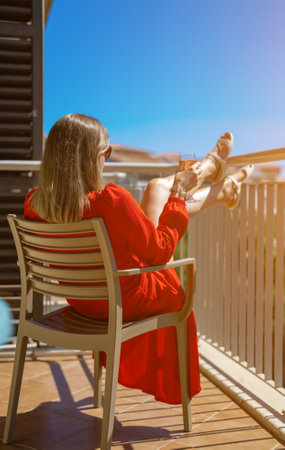 Woman in red dress with white wine enjoying vacation at balcony.の写真素材