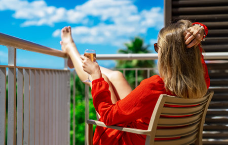 Woman in red dress with white wine enjoying vacation at balcony.の写真素材