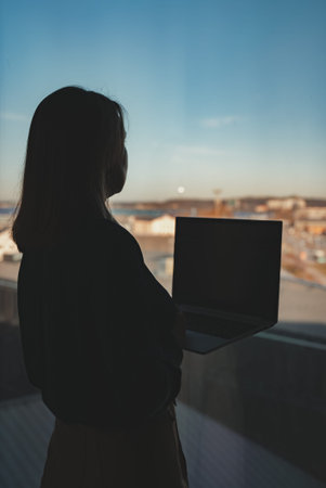 Silhouette of a woman with a laptop by the window.