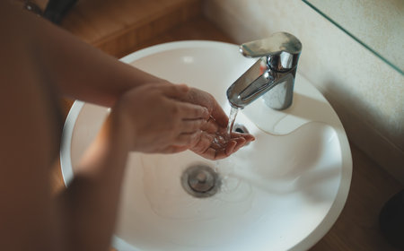 Woman washes her hands in the sink.の写真素材