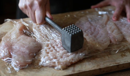 Tenderizing raw chicken fillet meat with mallet.