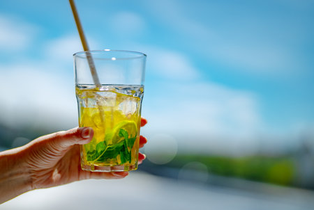 Hand holding refreshing yellow lime mint summer cocktail.の写真素材
