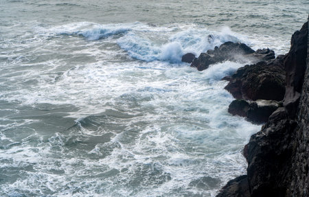 Powerful ocean waves crashing against dark volcanic rocks.