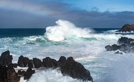 Massive ocean wave exploding against volcanic rocks.