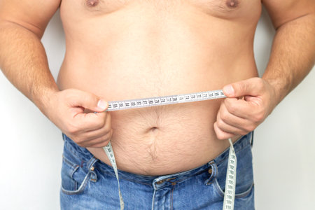 Fat man with big stomach wering jeans holding his measuring tapeの写真素材