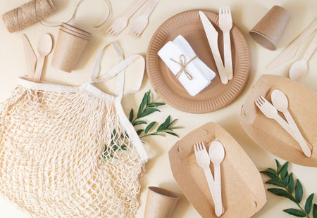 Zero waste, plastic-free and eco-friendly living. Paper disposable tableware, wooden cutlery and cotton mesh bag top view on beige tableの写真素材
