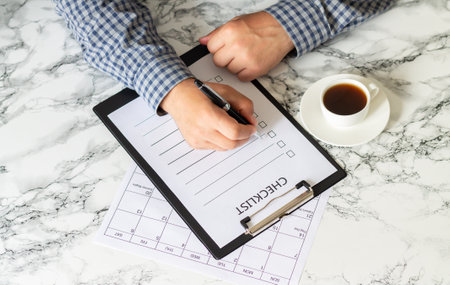 Man writing checklist next to cup of coffee on office table top viewの写真素材