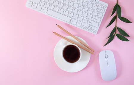 Female office workplace with keyboard, computer mouse, cup of coffee and plant on pink background. Flat lay, top viewの写真素材