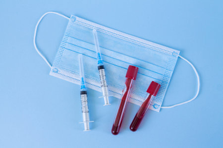 Blood test tubes, antiviral medical mask and syringe on blue background. Health protection and diagnostic conceptの写真素材