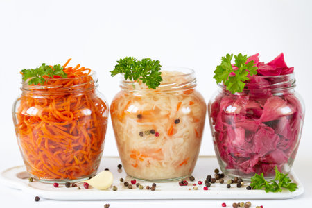 Fermented and preserved vegetarian food concept. Sauerkraut, marinated red cabbage and carrot in open glass jars on ceramic boardの写真素材