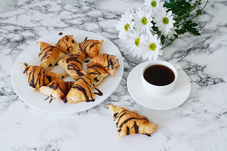 Flat lay of fresh chocolate buns, flowers and cup of coffee on marble background