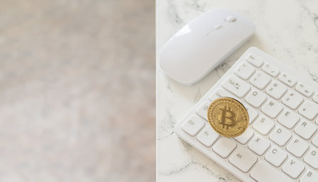 Cryptocurrency gold bitcoin on white computer keyboard next to mouse on marble tableの写真素材